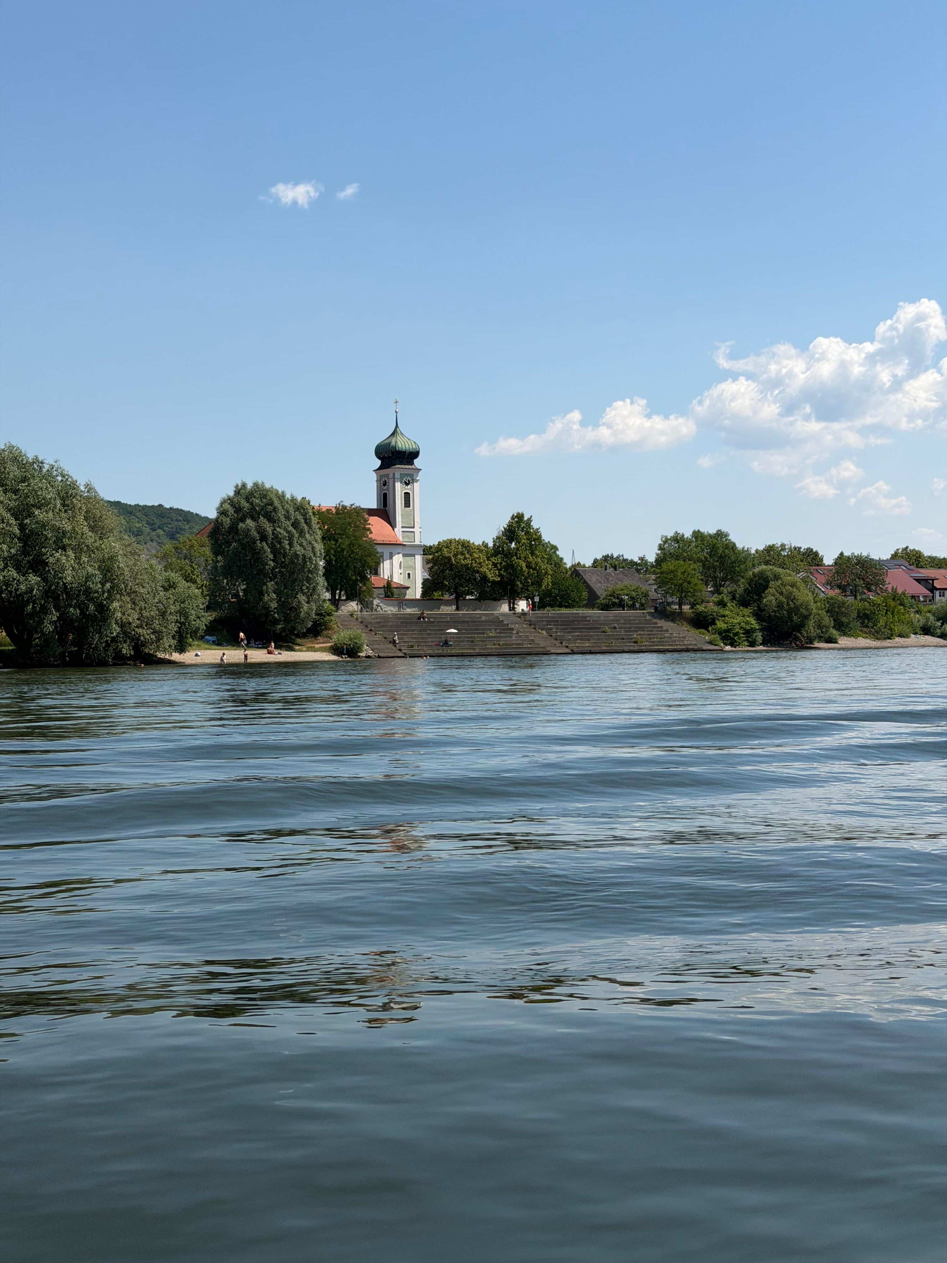Bayerisches Donaudorf mit Zwiebelturmkirche und Kiesstrand, Blick vom Floss während einer Flossfahrt