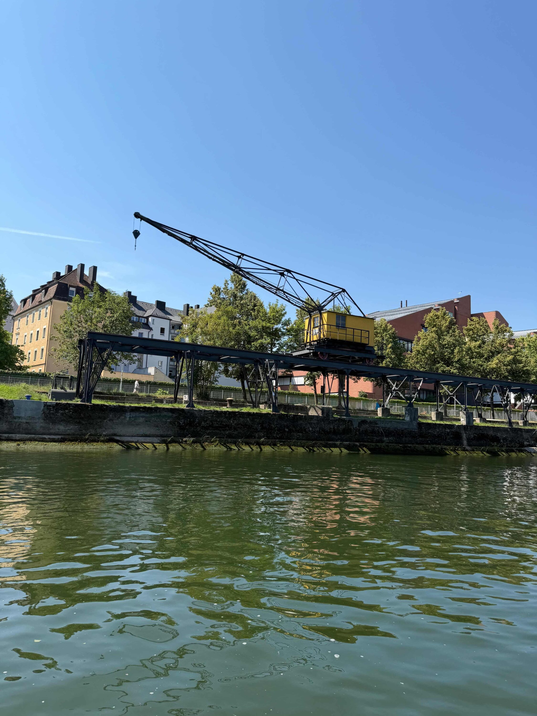 Historischer gelber Hafenkran am Donauufer in Regensburg, Blick vom Floss während einer Flossfahrt mit FLOSSMEISTER